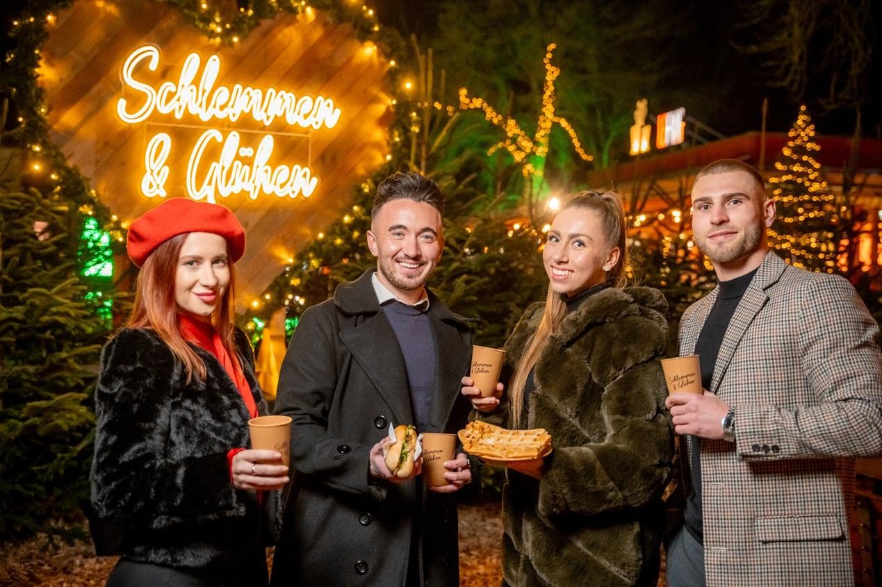 Guests with mulled wine in front of the Schlemmen & Glühen sign on the lake terrace